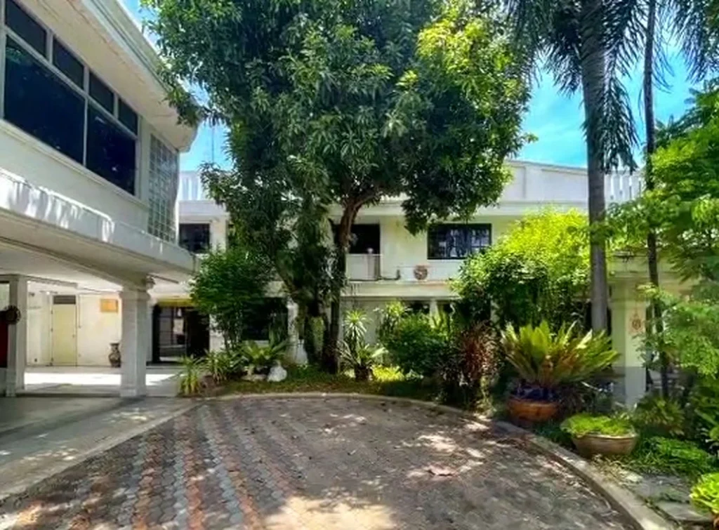 White office building and front courtyard surrounded by a garden and large trees