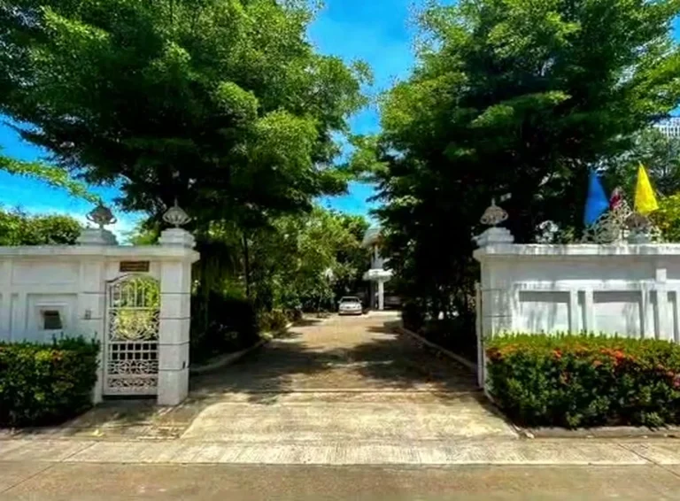 White gate and entrance to the land, shaded by large trees