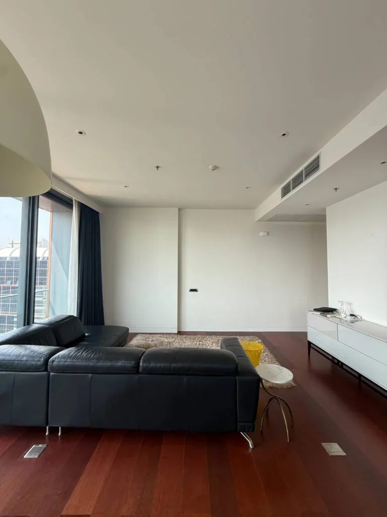 Living area with a black leather sofa, a white sideboard and a dark red-brown wood floor