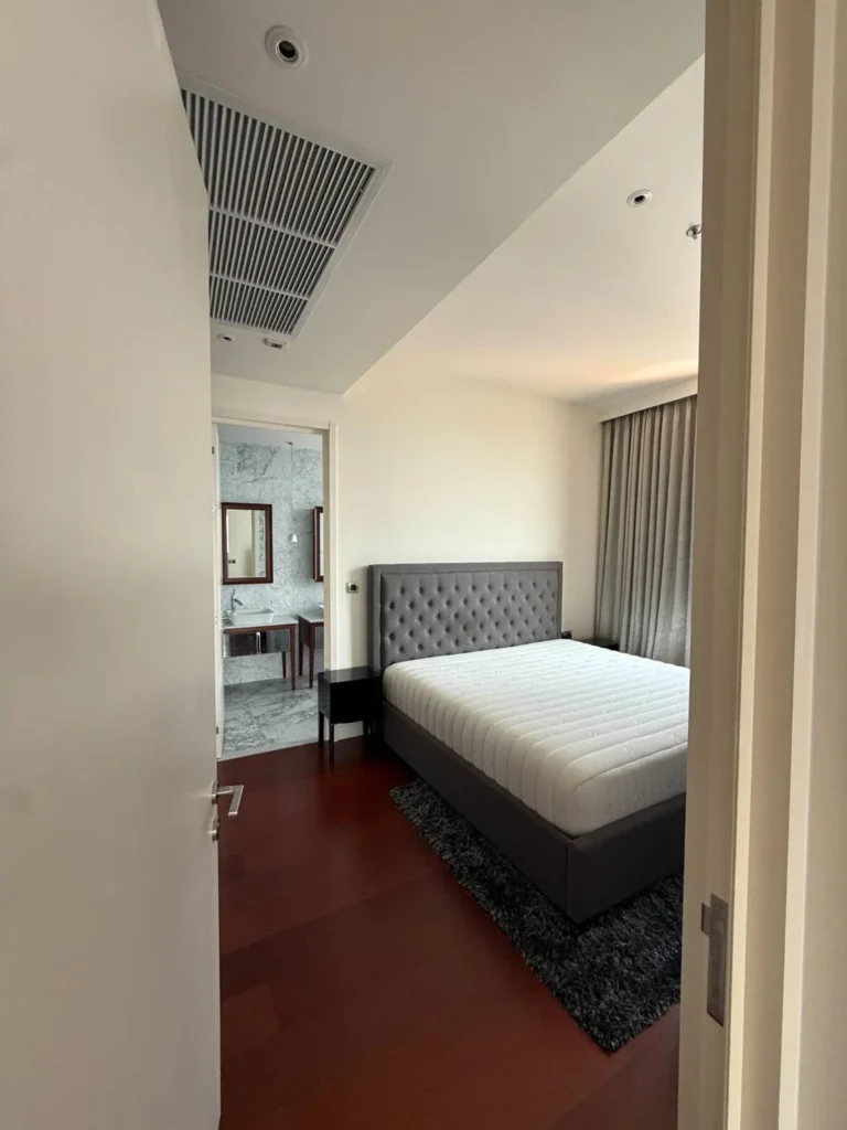 Master bedroom with a grey tufted headboard and a door to the marble bathroom