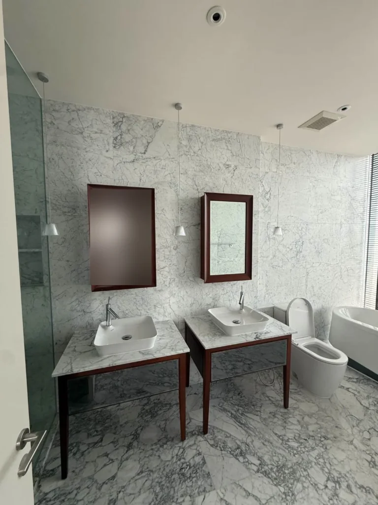 Marble bathroom with a double vanity, wood-framed mirrors and a freestanding bathtub
