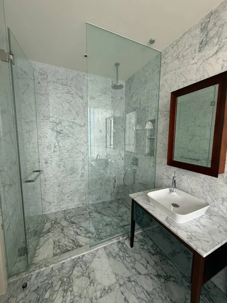 Glass walk-in shower with a rain shower and marble walls