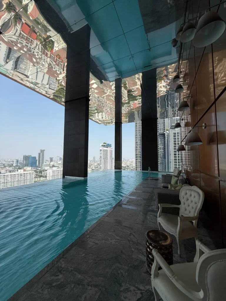 Infinity pool under a mirrored ceiling, with lounge chairs and the city skyline