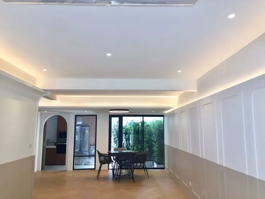 Open-plan living and dining room with a herringbone wood floor, white panelled walls and concealed ceiling lighting