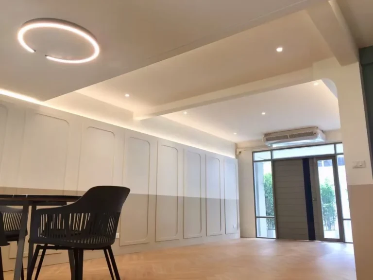 Living room looking towards the entrance, with a ring pendant light, panelled walls and an air conditioner