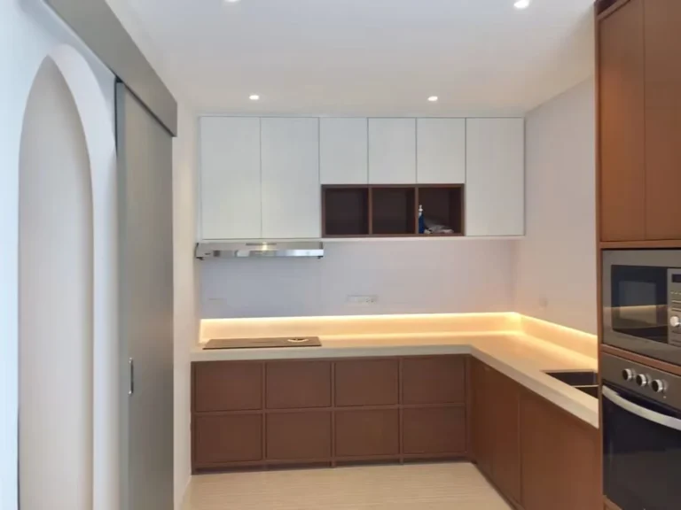 L-shaped kitchen with wood-tone lower cabinets, white upper cabinets, under-cabinet lighting and a cooker hood